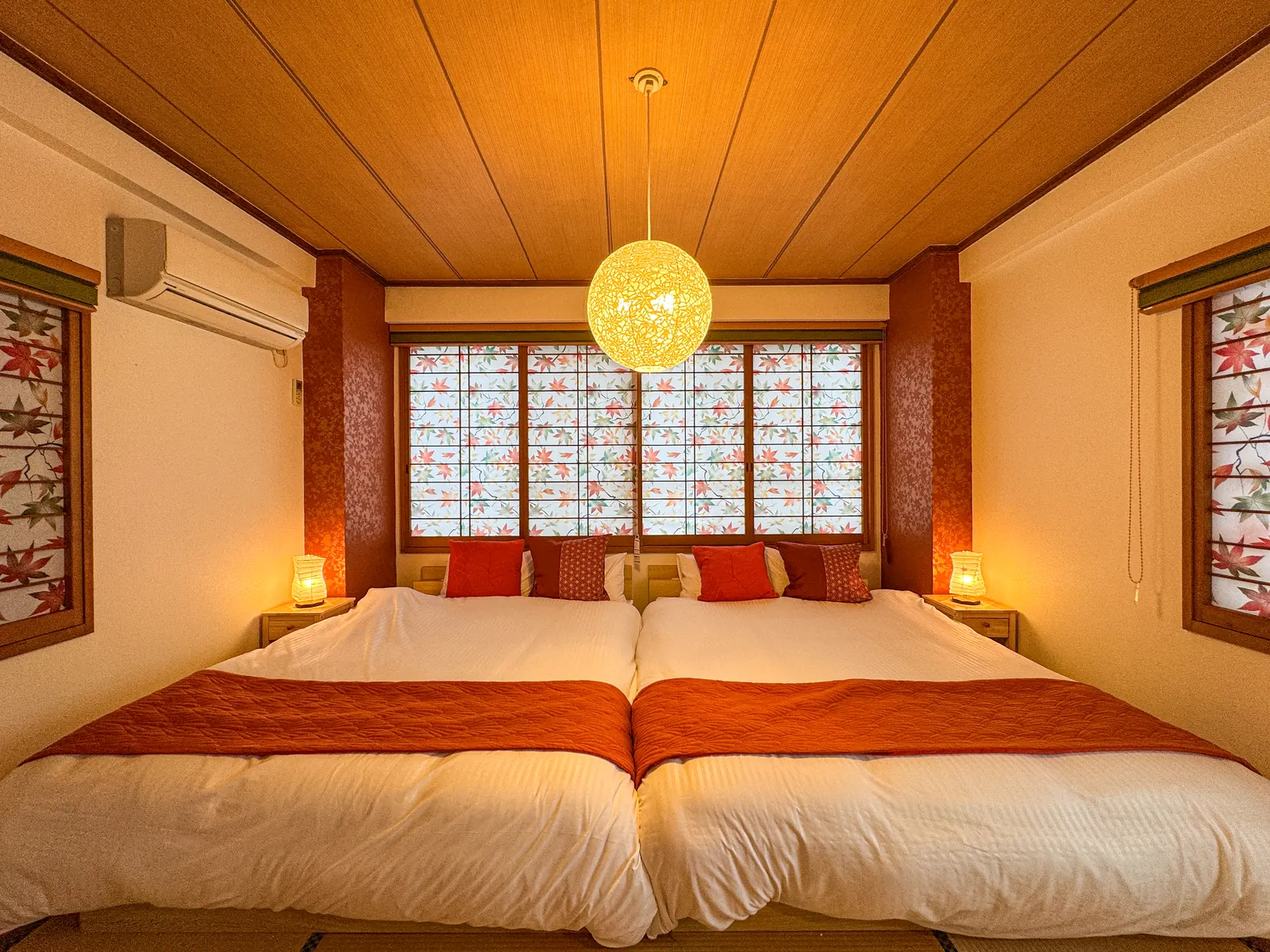 Tatami bedroom at Shibuya Nishikawa Stay with two double beds made up side by side, maple-leaf shoji screens across the window, a washi paper pendant lamp and two paper lamps on wooden nightstands